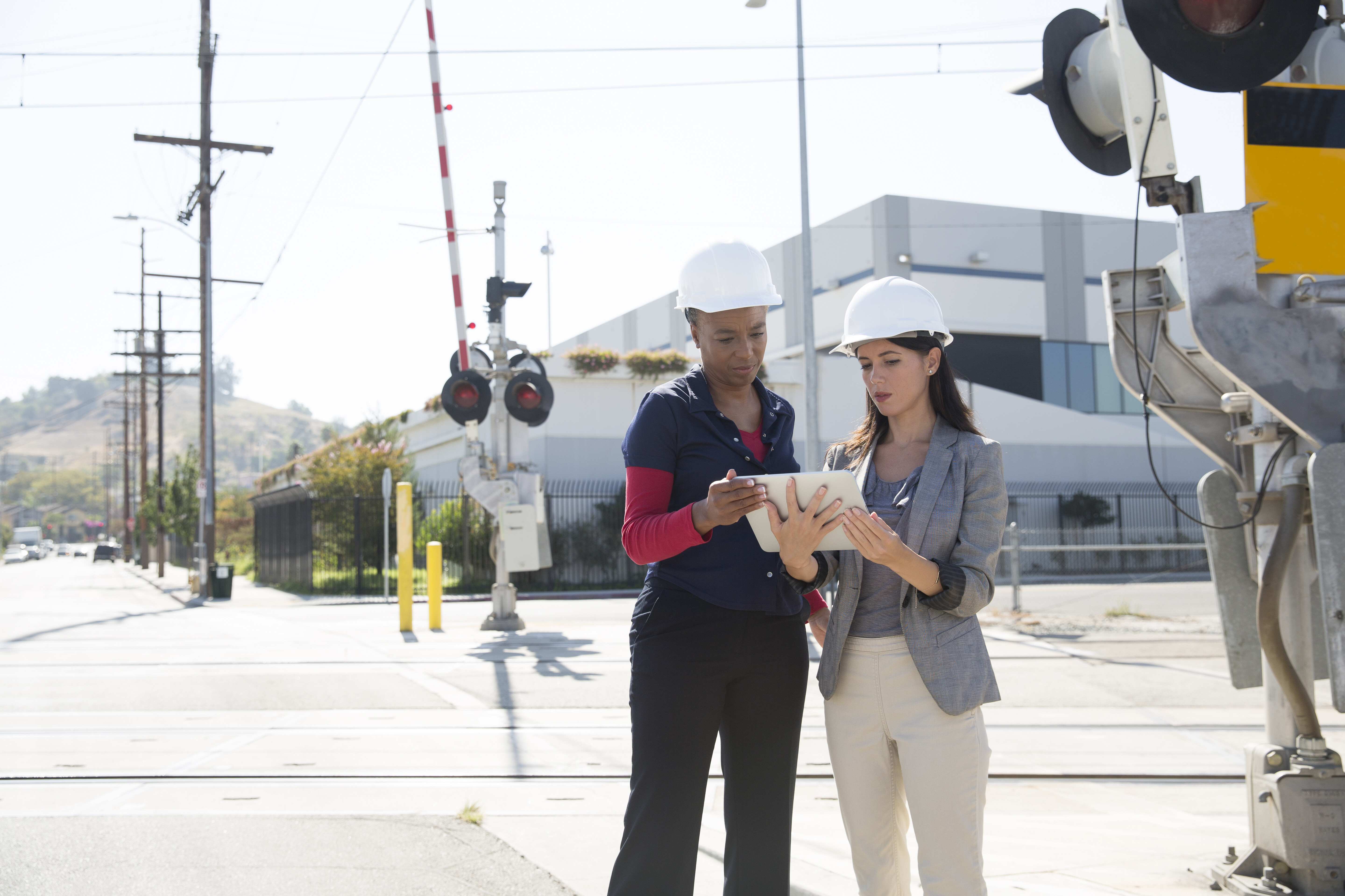 Two females with hard hats look at a clipboard outside of a job site.